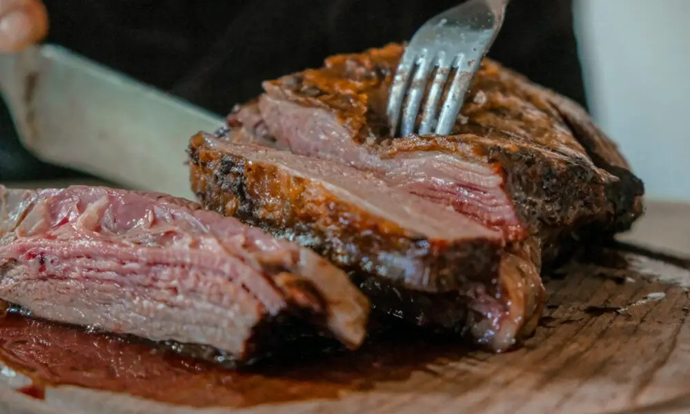person slicing a meat on brown wooden board