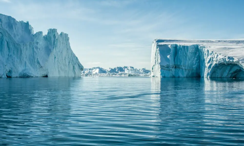 icebergs on body of water under blue and white sky at daytime
