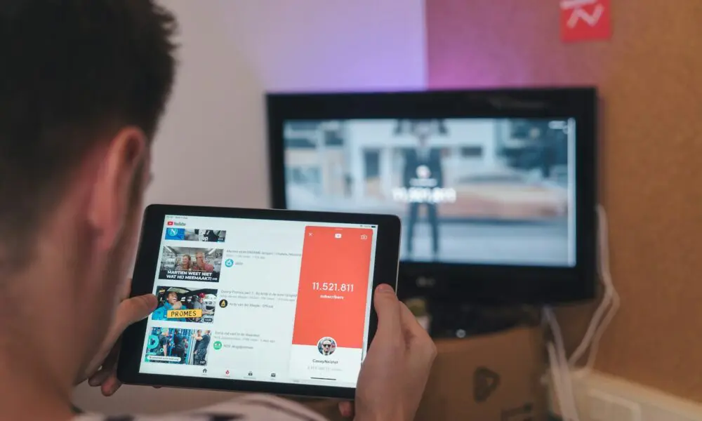 man browsing tablet sitting in front of TV