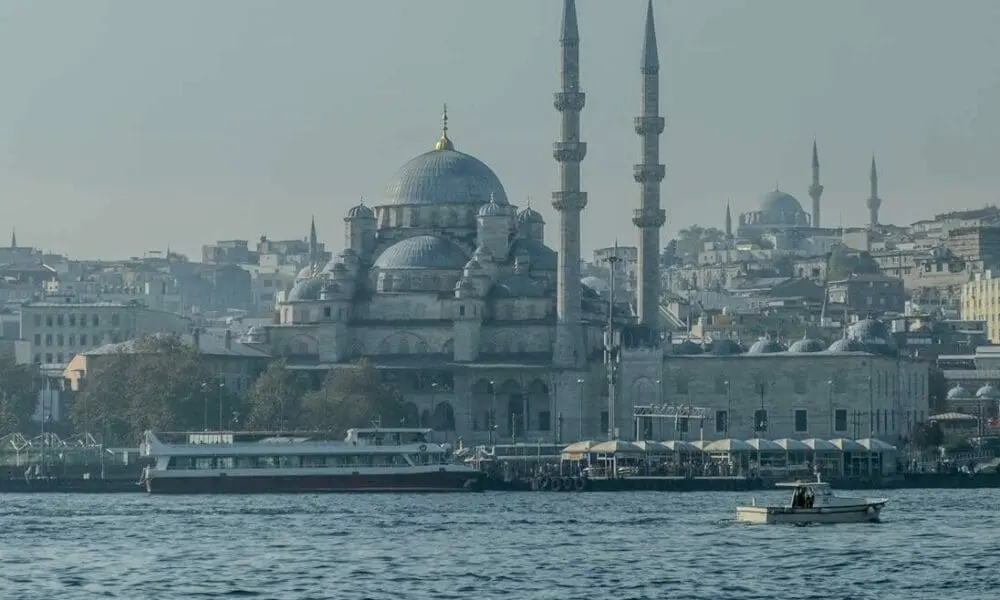 A serene view of the New Mosque in Istanbul with a background of city skyline and boats on the water.