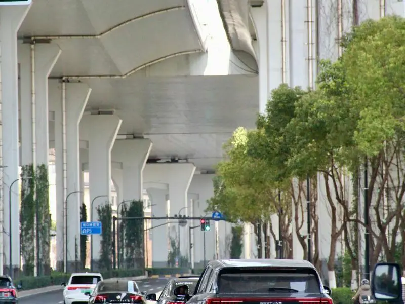 Cars driving under elevated highway in Shanghai, China during daytime.