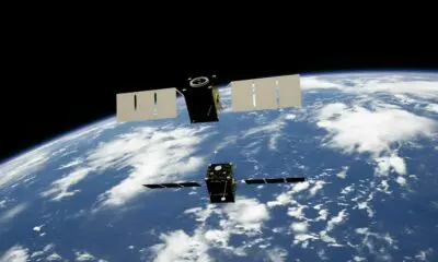 Two satellites with solar panels orbiting above the blue Earth with white clouds