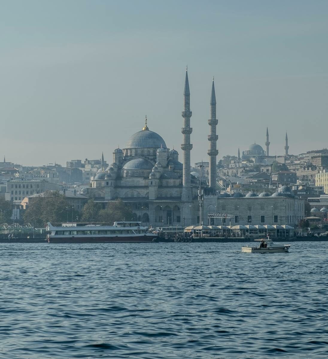 A serene view of the New Mosque in Istanbul with a background of city skyline and boats on the water.